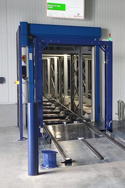 View of a blue automated pallet system entrance in a warehouse, featuring a monitor displaying above the system