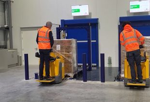 Two warehouse workers operating pallet trucks to load goods into an automated storage system
